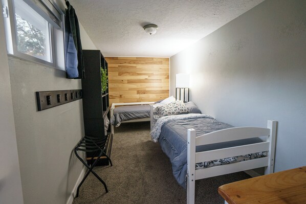A small, compact bedroom with two single beds, a desk, and a chair.