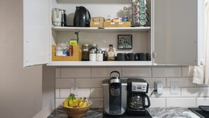 A kitchen with a coffee maker, a kettle, and a bowl of bananas.