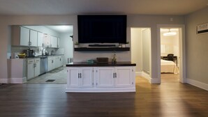 A modern kitchen with white cabinets, a black countertop, and a flat-screen TV mounted above the island.