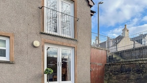 Una casa de dos pisos con un balcón, una puerta de madera y un muro de piedra.