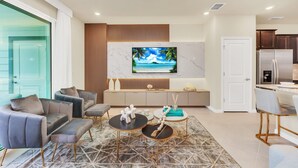 Ein modernes Wohnzimmer mit Fernseher, Sofas, einem Couchtisch und einer Küchenzeile inklusive Kühlschrank und Schränken.