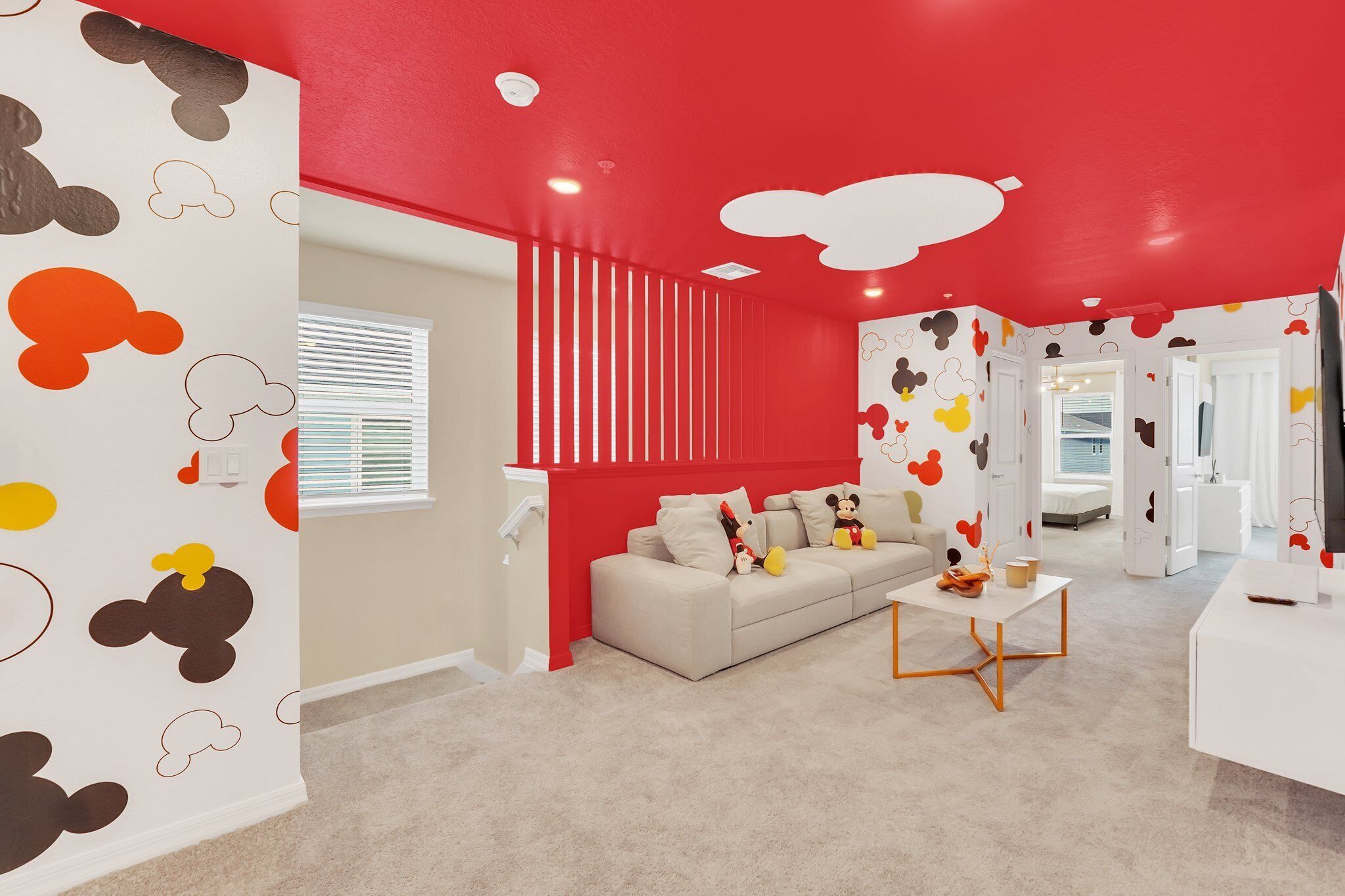 Ein Zimmer mit roter Decke, weißen Wänden mit Zeichentrickfiguren, einem beigen Sofa und einem kleinen Tisch mit einer Tasse.