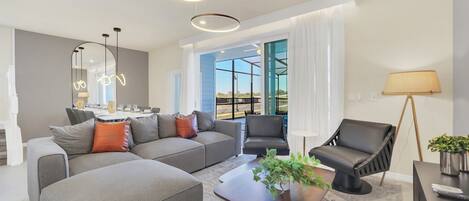A modern living room with a grey sofa, a black armchair, and a coffee table with a plant. There is a dining area in the background with a table and chairs.