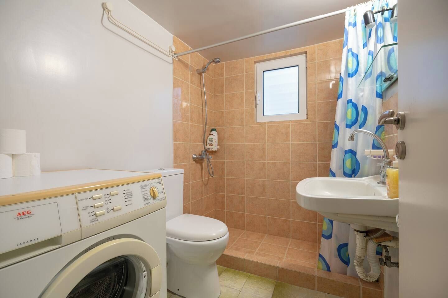 A compact bathroom with a washing machine, toilet, shower, and sink.