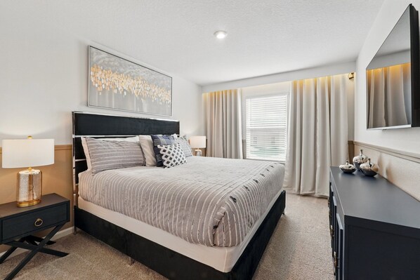 A modern bedroom with a large bed, a nightstand, a dresser, and a wall-mounted TV. - EV_2379 - 5BR / 4BA Villa w/ Private Pool, Loft, Resort Access & Themed Rooms (Kissimmee)