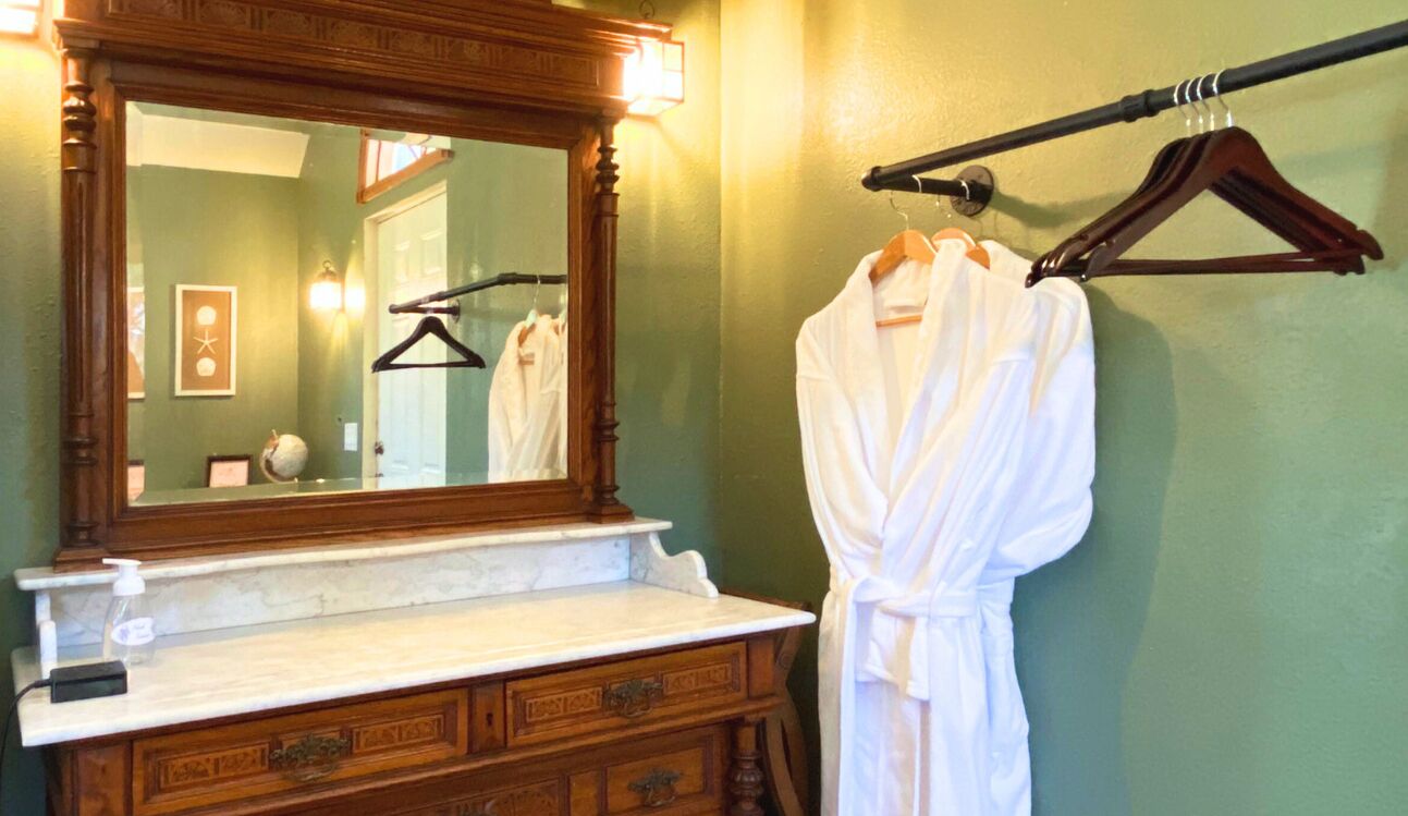 A bathroom with a wooden vanity, a large mirror, and a robe hanging on a rack.