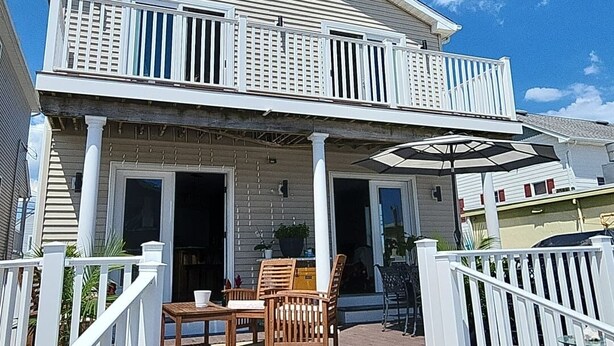 Une maison à deux étages dotée d’un porche abrité, d’un coin repas avec des chaises et une table, et d’un petit jardin.
