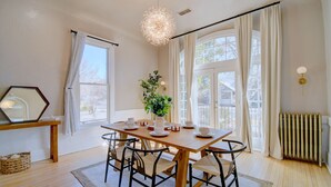 Un coin repas avec une table en bois, des chaises, un vase avec une plante et une grande fenêtre avec des rideaux.