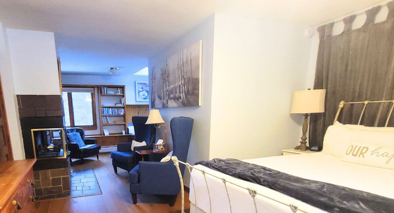 A hotel room with a bed, a desk, a chair, a bookshelf, and a painting on the wall.