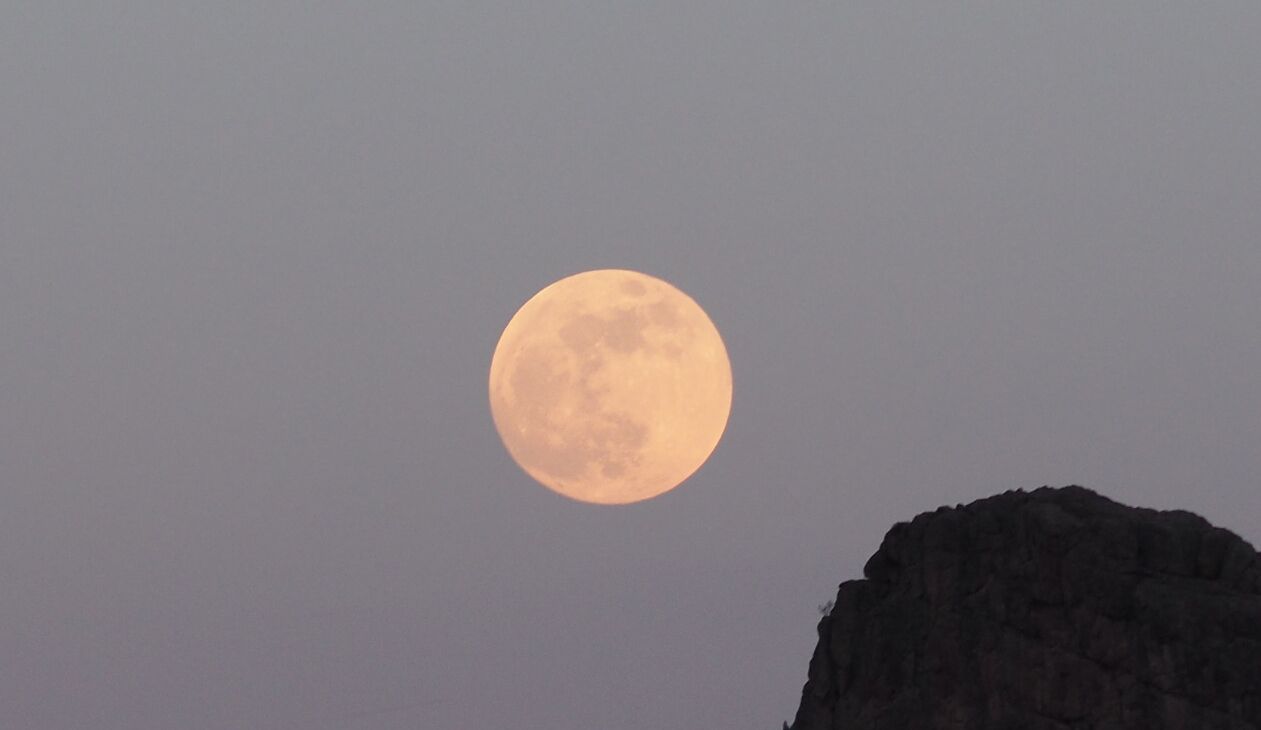 Une pleine lune dans le ciel, avec une formation rocheuse en premier plan.