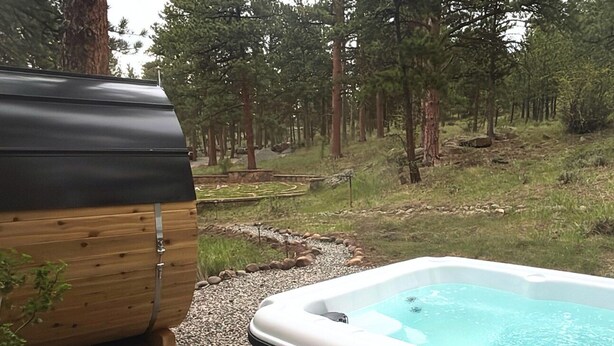 A hot tub surrounded by a forested area with a wooden structure nearby. - Priaire Sage Room at RiverSong Inn in Estes Park - Riverside in Rocky Mountain National Park (Estes Park)