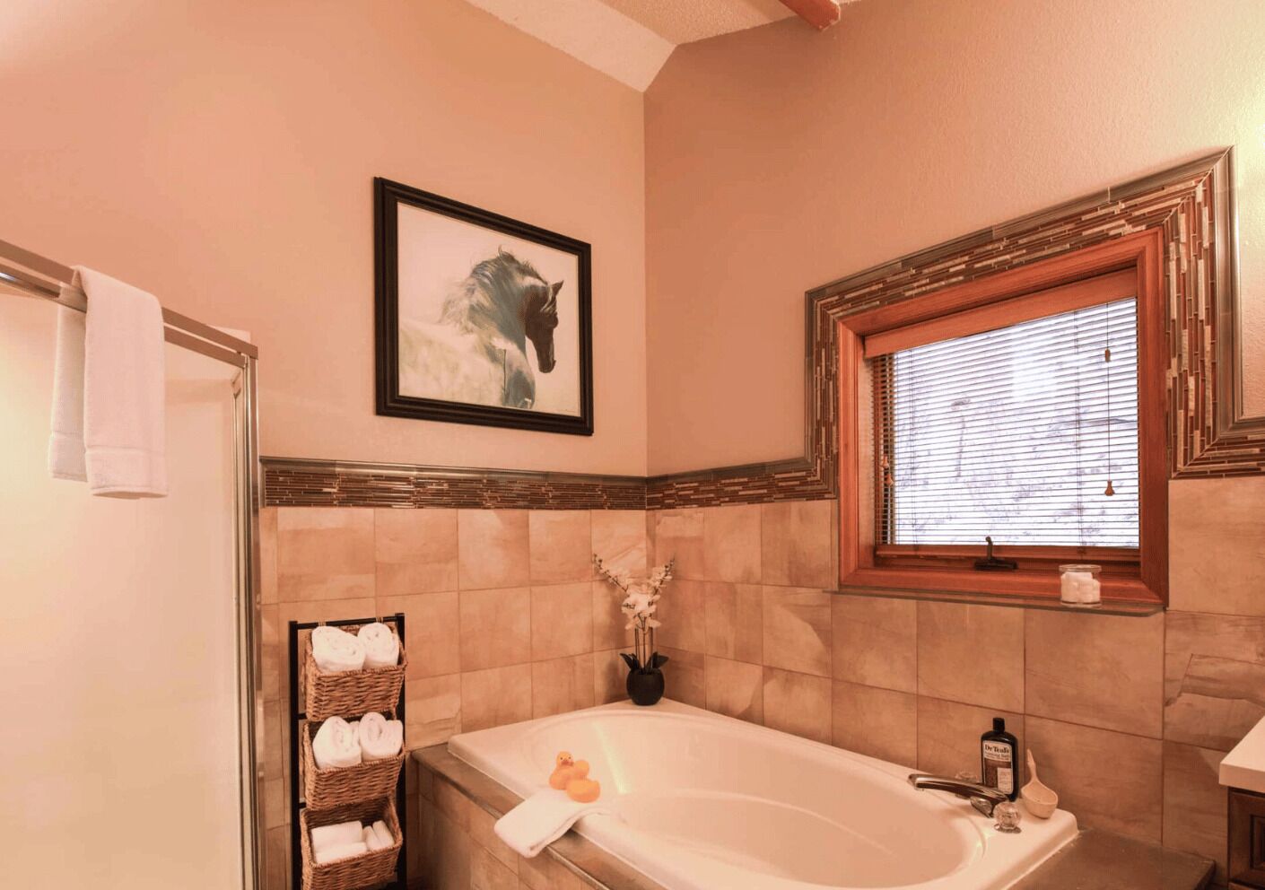 Un bagno con una vasca, una finestra con persiane, un quadro appeso al muro e un portascopevoli con asciugamani.
