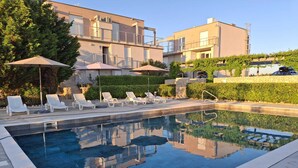 A swimming pool with lounge chairs and umbrellas, surrounded by buildings and greenery. - Quiet 79m2 apartment by the sea with garden and communal pool (Povljana)