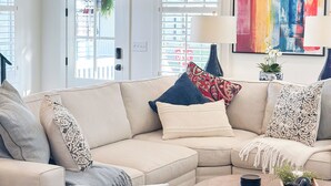 A modern living room with a beige sectional sofa, a round coffee table, and a colorful abstract painting on the wall.