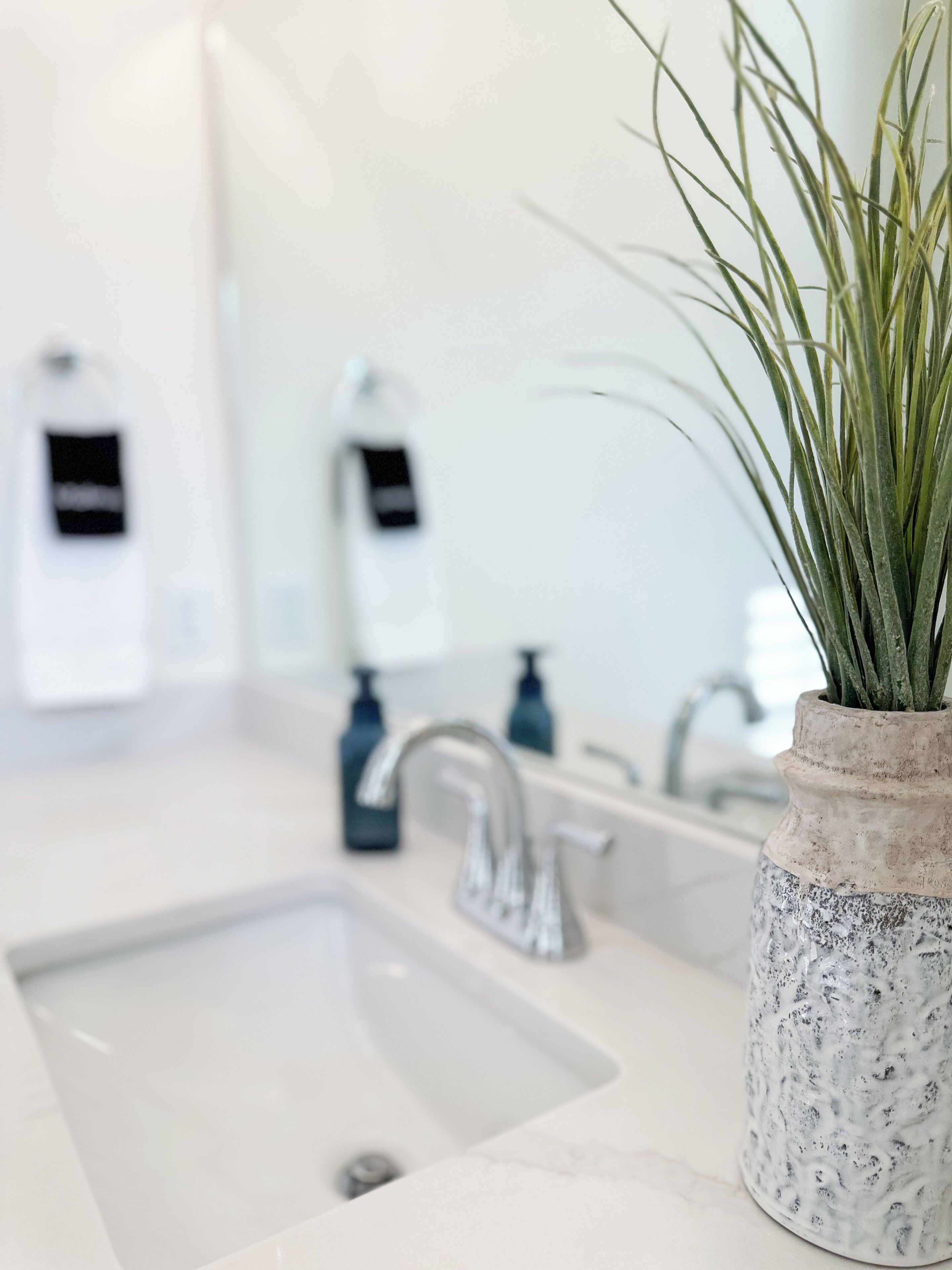 A bathroom with a white sink, a mirror, and a plant in a textured vase.