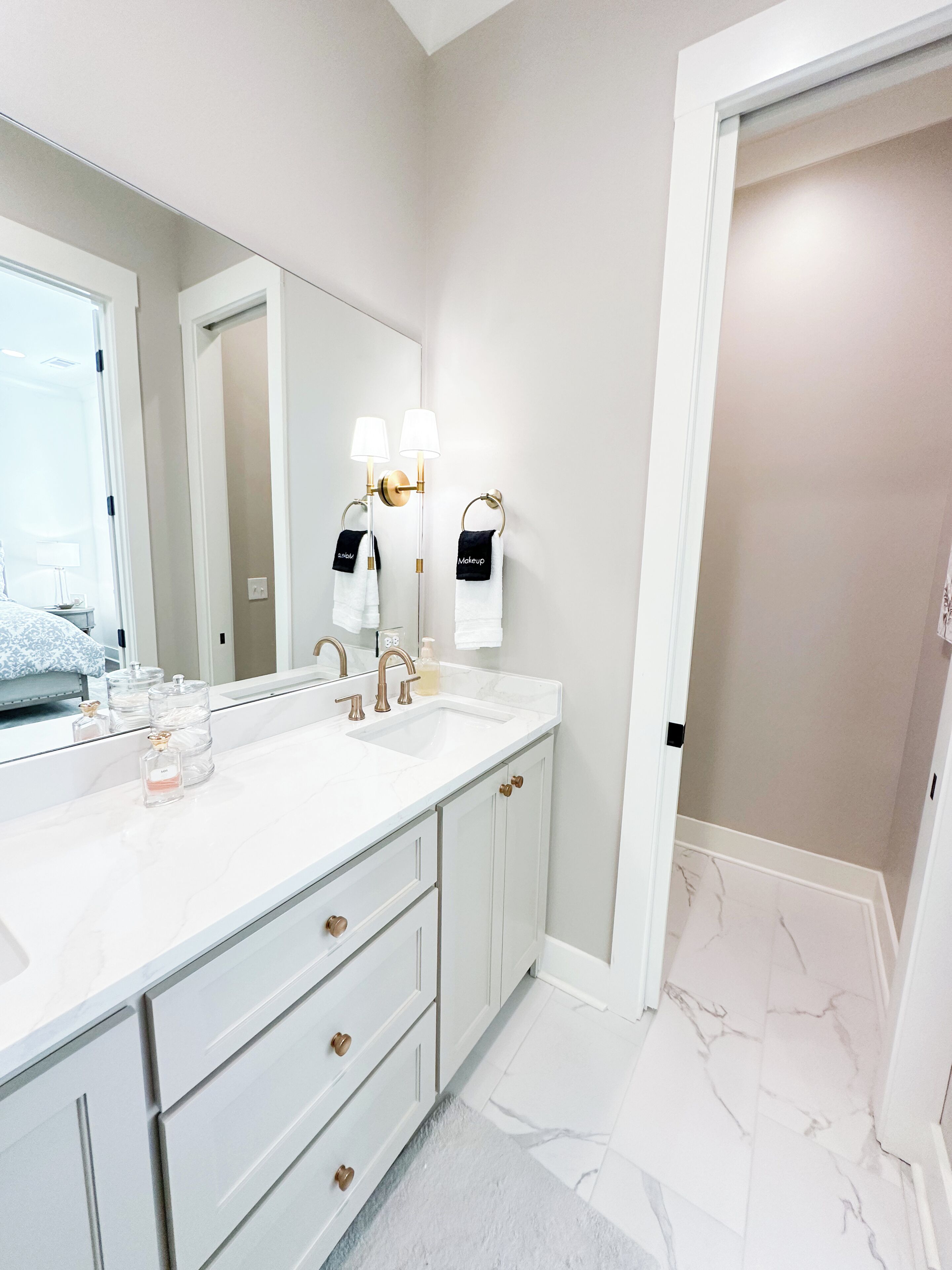 Un baño moderno con un tocador blanco, dos lavamanos, un espejo grande y un vestidor.