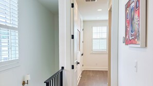 A hallway with a wooden floor, white walls, a black railing, and a painting on the wall.