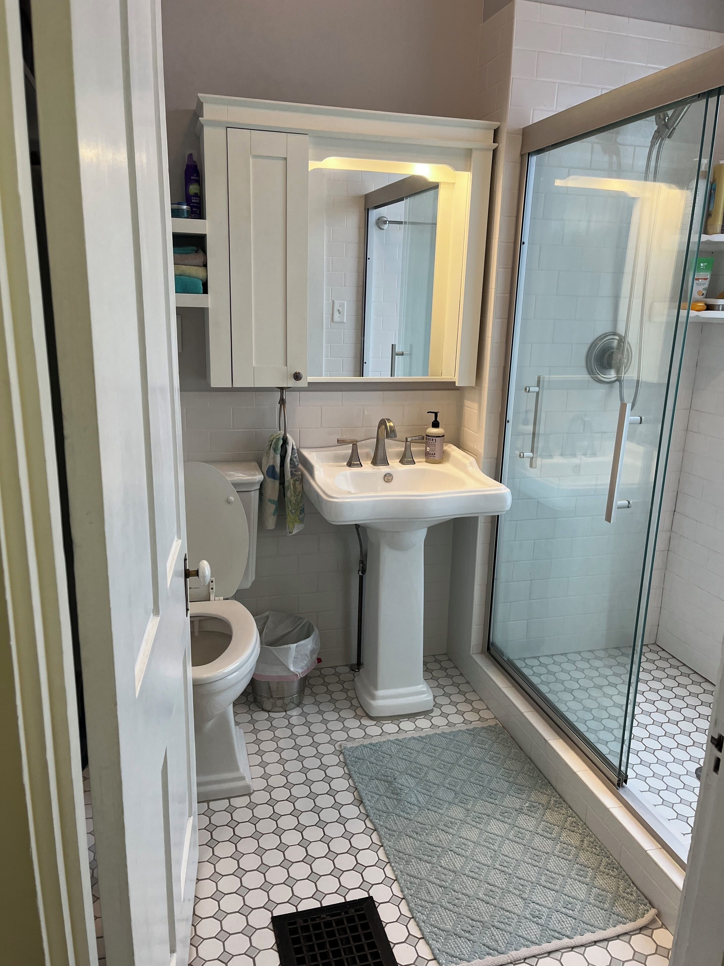 Une salle de bain avec un lavabo sur colonne blanc, des toilettes, une douche en verre et un sol carrelé.