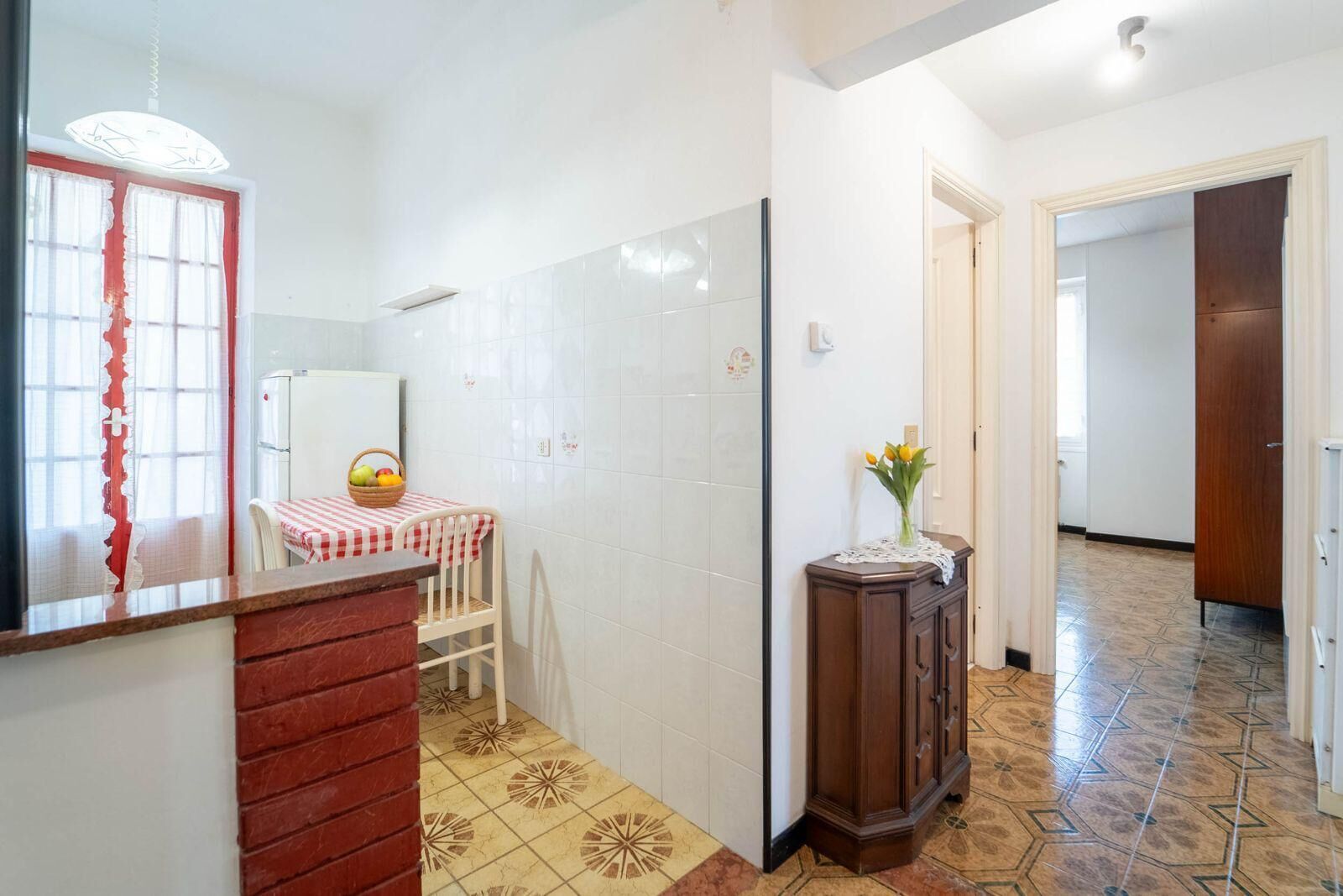 A kitchen with a red and white checkered tablecloth, a wooden cabinet, and a tiled floor.