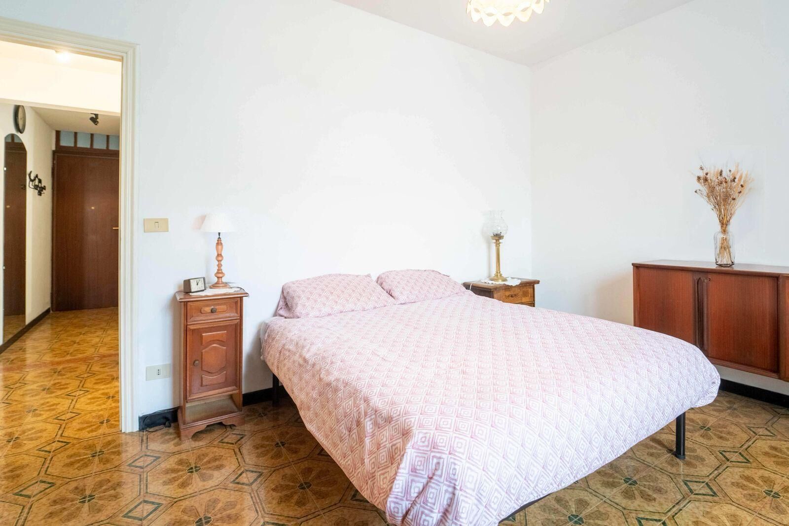Un dormitorio con cama, mesita de noche, cómoda y una puerta que da a otra habitación.