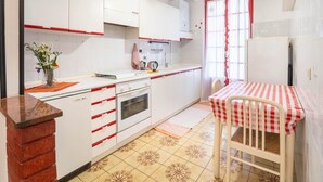 Una cocina compacta con armarios blancos, una mesa a cuadros roja y blanca, y piso de baldosas.