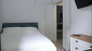 A bedroom with a bed, a TV mounted on the wall, and a door leading to another room.