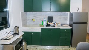 A kitchen with green cabinets, a stainless steel refrigerator, and a countertop with various items.