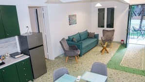 A compact living space with a kitchenette, a teal sofa, two armchairs, and a glass dining table.