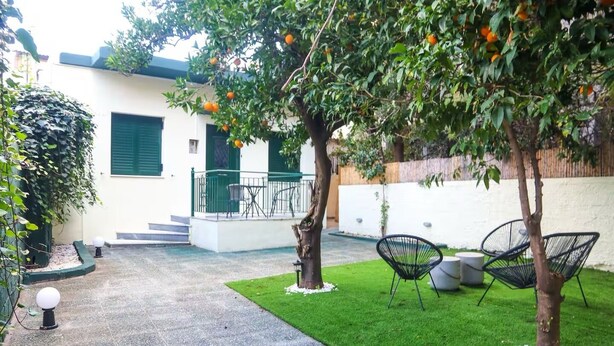 A courtyard with artificial grass, two chairs, a tree with oranges, and a building with a balcony.