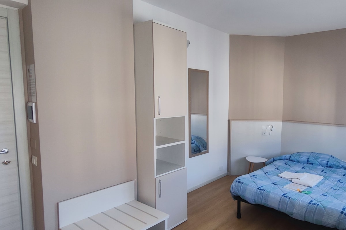 A bedroom with a bed, a wardrobe, a bedside table, and a small stool.
