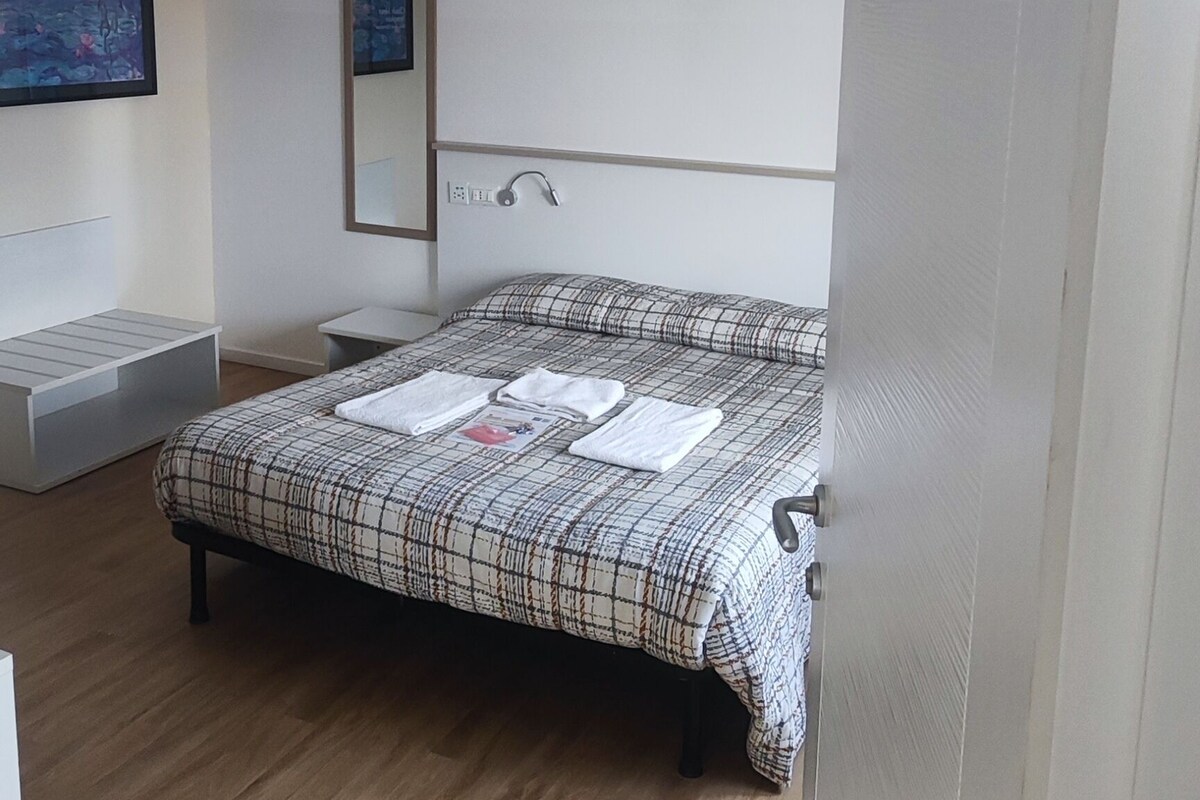 A bedroom with a bed, a bedside table, a mirror, and a wall-mounted TV.