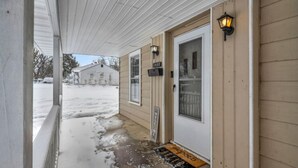 A covered porch with a wooden door, a welcome sign, and a mailbox.
