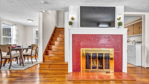 A living room with a fireplace, wooden staircase, and a dining area with chairs and a table.