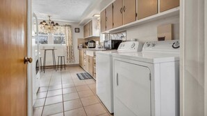 A kitchen with a washing machine, a microwave, and a sink. There are stools and a window with curtains.