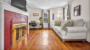 A living room with a fireplace, a sofa, a TV, and a window with curtains.
