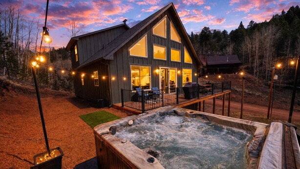 Una cabaña con jacuzzi, mobiliario exterior e iluminación con guirnaldas.