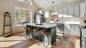 Una cocina moderna con una isla grande, taburetes de bar y vistas a un bosque.