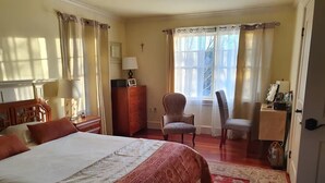 A bedroom with a large bed, a chair, a desk, and a window with curtains.