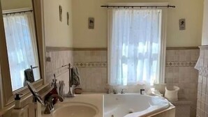 A bathroom with a sink, mirror, vanity, bathtub, and a window with a curtain.