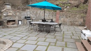 A patio with stone tiles, a table with chairs, a blue umbrella, and a brick wall.