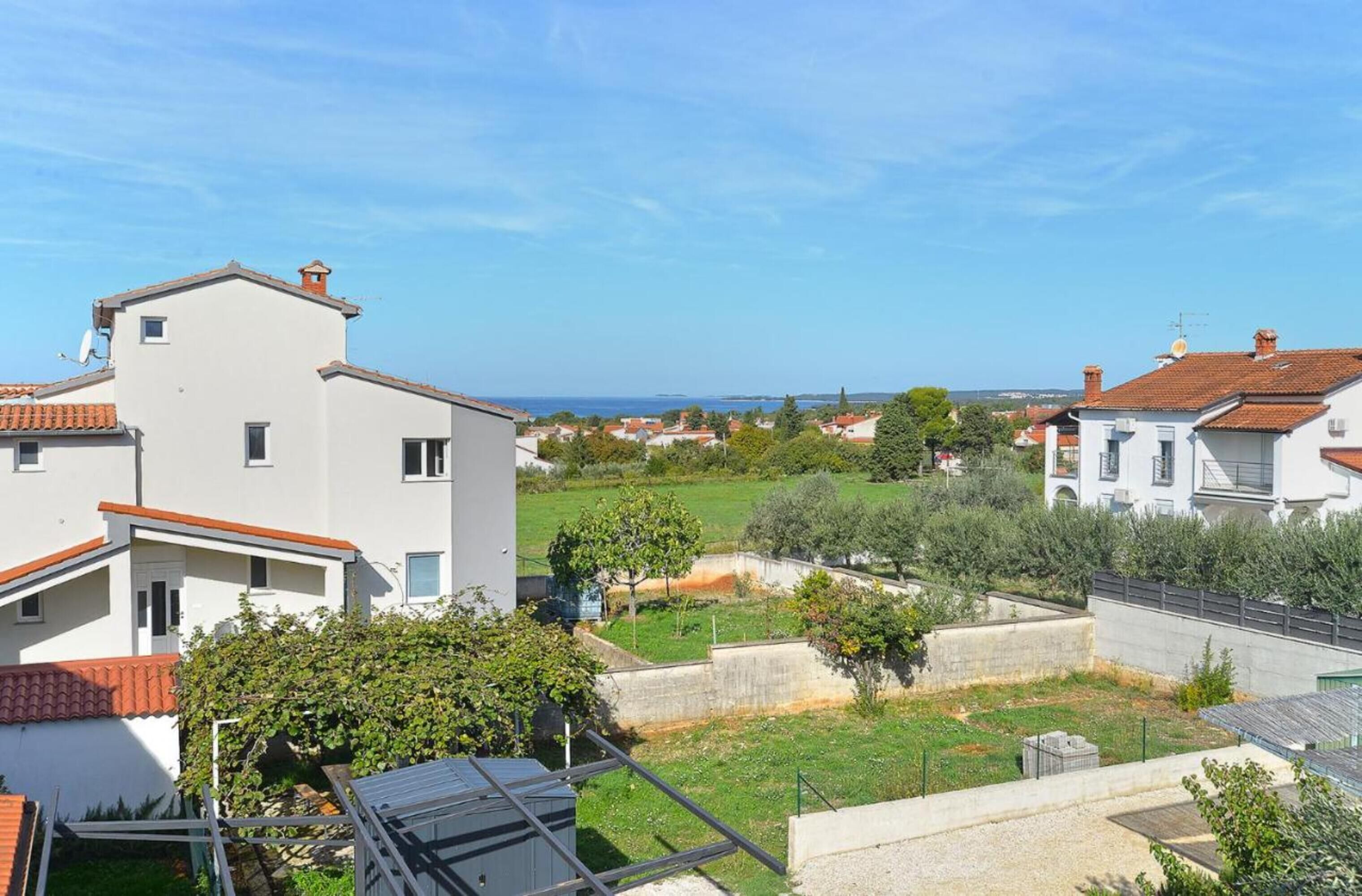 A residential area with white buildings, a clear blue sky, and a view of the sea.