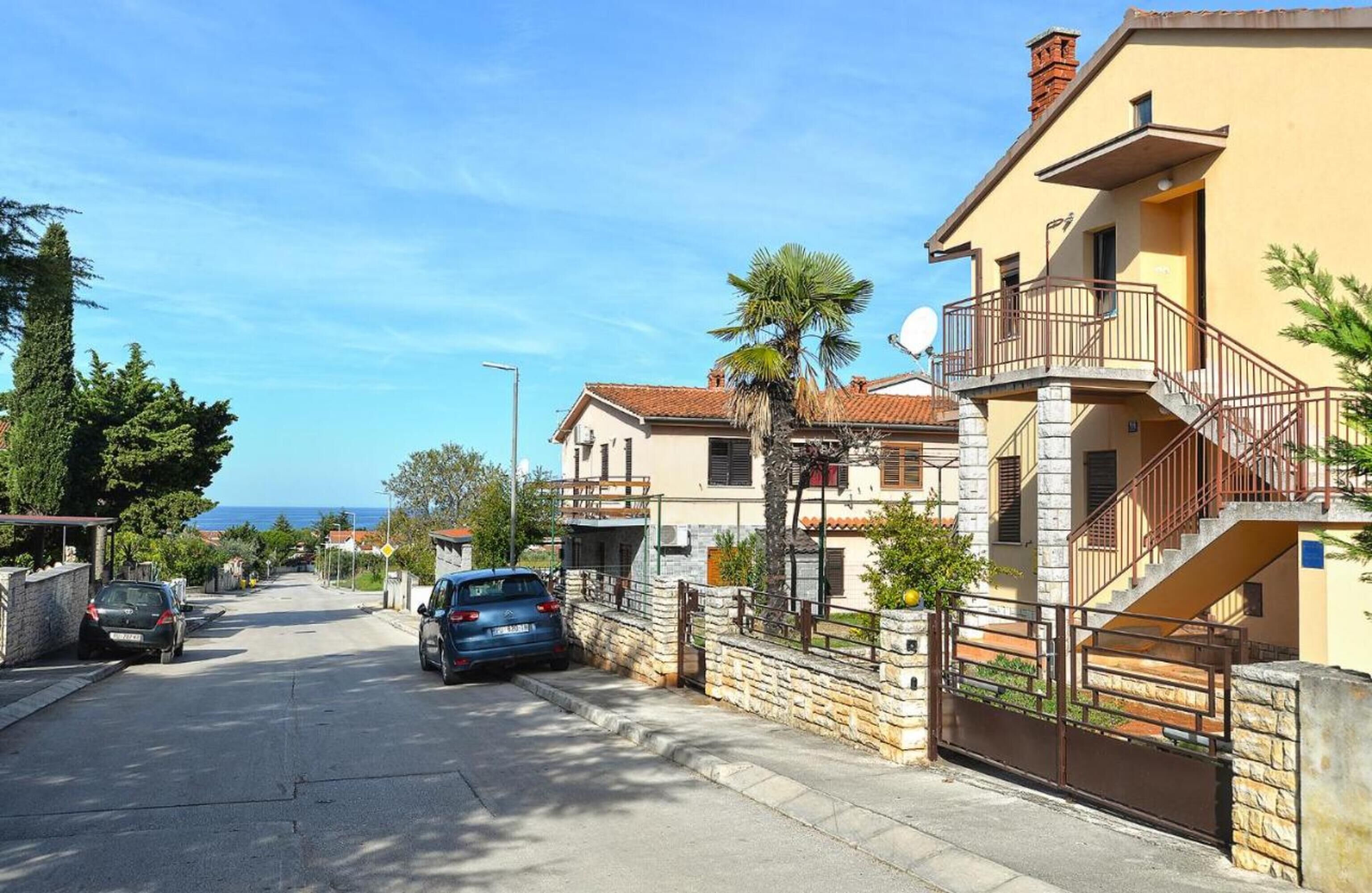 A residential street with houses, a parked car, and a clear view of the sea in the background.