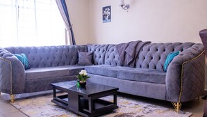 Ein graues, bezogenes Sofa mit goldfarbenen Akzenten, ein schwarzer Couchtisch und ein gemustertes Teppich.