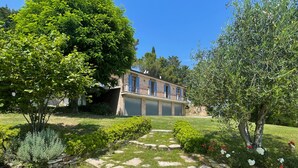 Ein zweistöckiges Haus mit einem steinbelagten Weg zum Eingang, umgeben von üppiger Bepflanzung und blühenden Pflanzen.