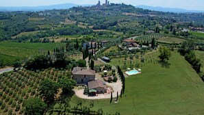 Vue aérienne d’un domaine rural comprenant des vignobles, une piscine et une grande maison en pierre entourée de verdure.