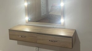 Un meuble-lavabo avec un miroir et des lampes, un meuble à tiroirs en bois en dessous, et un sol carrelé.