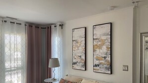 Ein Schlafzimmer mit einem Bett, zwei an der Wand befestigten abstrakten Bildern, einem Nachttisch mit Lampe und einem Fenster mit Vorhängen.