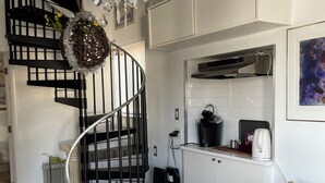 Eine moderne Küche mit weißen Schränken, einer schwarzen Wendeltreppe, einem Chandelier und einem Essbereich mit rundem Tisch und Stühlen.