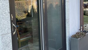 Eine moderne Schiebetür aus Glas mit einem Metallgriff, eingelassen in eine Steinwand, neben der sich ein kleiner Pflanztopf befindet.