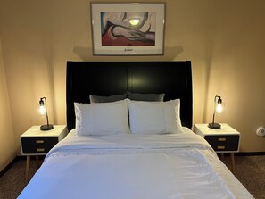 A neatly made bed with white linens, two bedside lamps, a framed artwork above the bed, and a dark headboard. - Charming 4-bedroom house with AC, WiFi. 10 mins to WSU (Kechi)